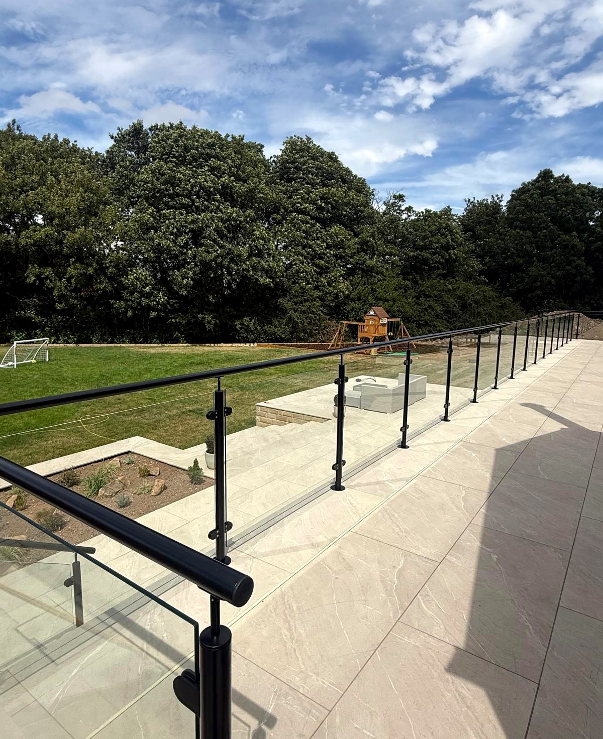 Galvanised and powder-coated glass balustrade along a porcelain patio with steps down to the garden, Sheffield